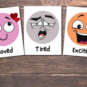May include: Three cards with cartoon faces representing emotions. The first card shows a pink face with hearts and the word "Loved". The second card has a gray face and the word "Tired". The third card has an orange face and the word "Excited".