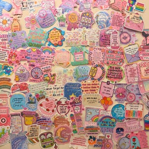May include: A collection of colorful stickers with various designs and inspirational quotes. The stickers feature illustrations of flowers, rainbows, and food items, with text like "Enjoy Every Moment" and "Time for Self Love."