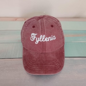 Op de afbeelding: Een oudroze baseballpet met het woord Fyllenia in wit schrijfschrift geborduurd op de voorpanelen. De pet heeft een constructie van zes panelen met bijpassende oogjes en een gebogen klep met zichtbare stiksels over het gehele oppervlak.