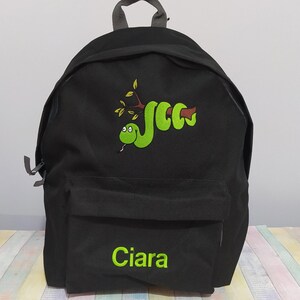 Peut inclure: Sac à dos noir avec un motif de serpent vert et le nom "Ciara" brodé en vert. Le serpent est enroulé autour d'une branche marron avec des feuilles vertes. Le sac à dos a une poche avant et une poignée supérieure.
