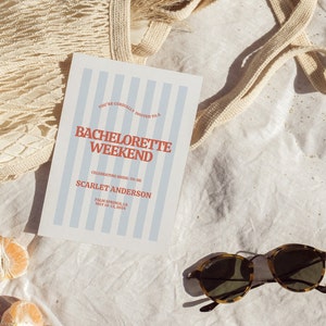 May include: A white card with blue stripes and red text announcing a bachelorette weekend for Scarlet Anderson in Palm Springs, CA from May 10-13, 2024. The card is lying on a white fabric surface with a tan mesh bag and two halved mandarin oranges.