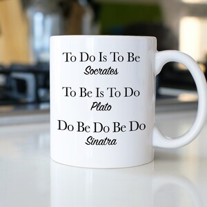 May include: White ceramic mug with black text that reads "To Do Is To Be Socrates", "To Be Is To Do Plato", and "Do Be Do Be Do Sinatra".