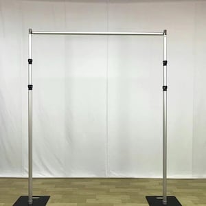 May include: A silver metal adjustable backdrop stand with a horizontal bar and two vertical poles. The stand has black square bases and adjustable black joints. The background is a white fabric.
