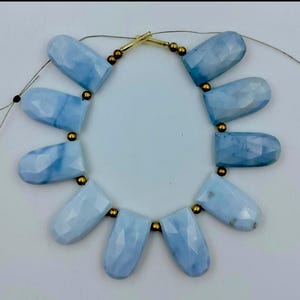 May include: A strand of light blue opal beads with gold spacers. The beads are faceted and have a teardrop shape. The strand is strung on a thin cord and has a clasp.