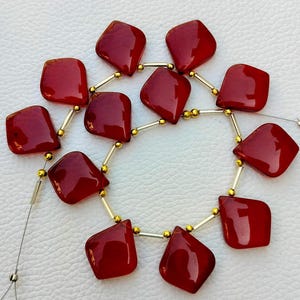 May include: A strand of red gemstone beads with a faceted, diamond-shaped design. The beads are strung on a silver wire with gold spacers.