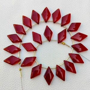 May include: A strand of 20 red gemstone beads in a diamond shape. The beads are strung on a gold wire.
