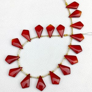 May include: A strand of red carnelian gemstone beads, each bead is faceted and shaped like a teardrop. The beads are strung on a gold-colored wire.