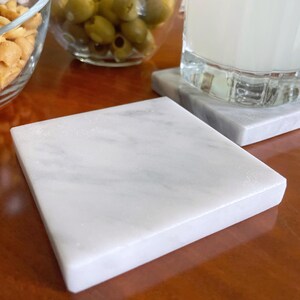 Sottobicchiere in marmo bianco Carrara dal design minimalista e raffinato. Superficie leggermente ruvida e angoli smussati. La forma quadrata e le dimensioni compatte li rendono perfetti per qualsiasi tipo di bicchiere, sia da vino che da cocktail.