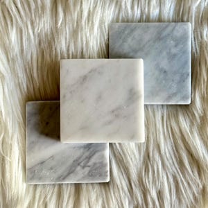 Sottobicchiere in marmo bianco Carrara dal design minimalista e raffinato. Superficie leggermente ruvida e angoli smussati. La forma quadrata e le dimensioni compatte li rendono perfetti per qualsiasi tipo di bicchiere, sia da vino che da cocktail.