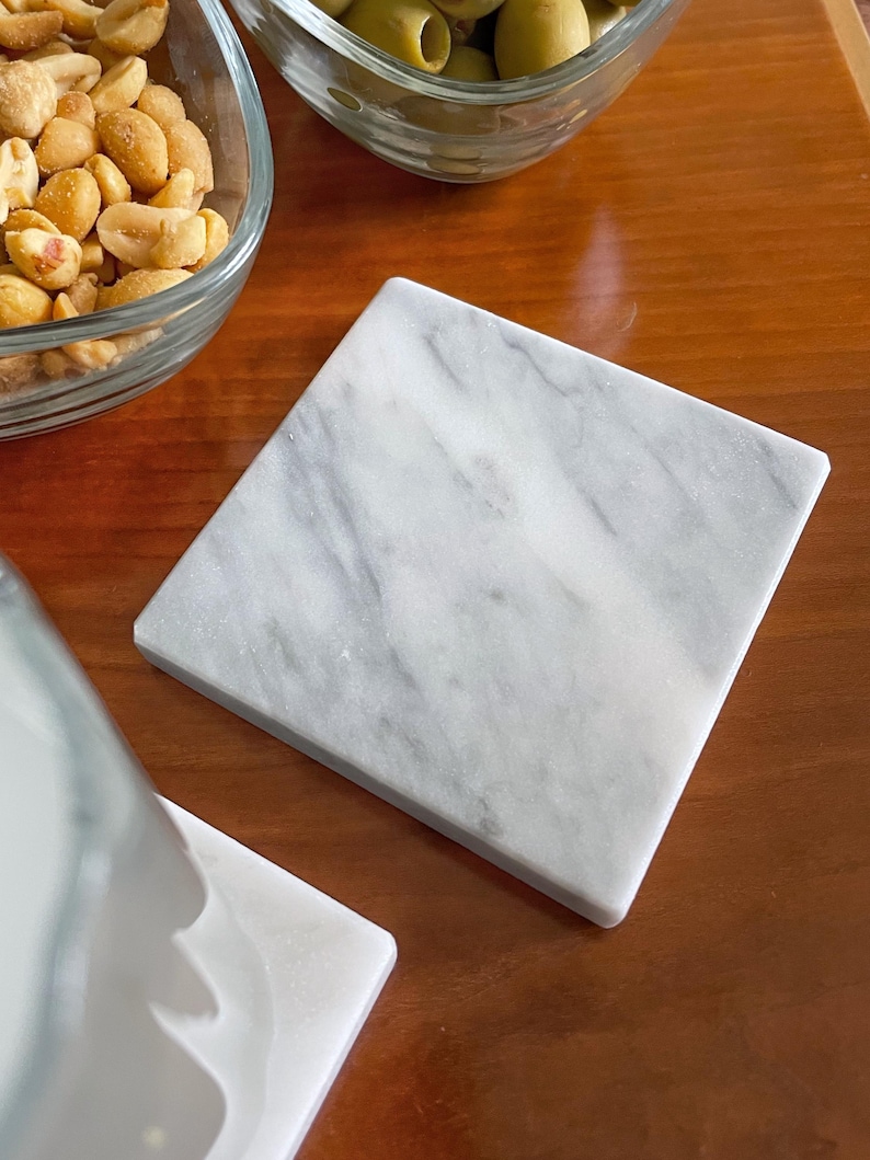 Sottobicchiere in marmo bianco Carrara dal design minimalista e raffinato. Superficie leggermente ruvida e angoli smussati. La forma quadrata e le dimensioni compatte li rendono perfetti per qualsiasi tipo di bicchiere, sia da vino che da cocktail.
