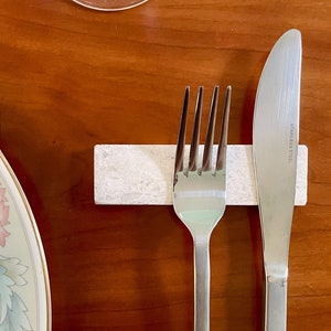 Questo poggiaposate è in marmo, con una tonalità beige chiara e una finitura leggermente ruvida. La superficie presenta leggere intrusioni e imperfezioni che conferiscono un aspetto rustico. La forma è rettangolare con bordi totalmente smussati.