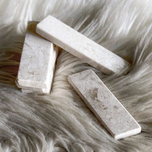 Questo poggiaposate è in marmo, con una tonalità beige chiara e una finitura leggermente ruvida. La superficie presenta leggere intrusioni e imperfezioni che conferiscono un aspetto rustico. La forma è rettangolare con bordi totalmente smussati.