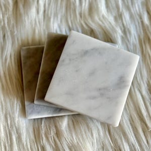 Sottobicchiere in marmo bianco Carrara dal design minimalista e raffinato. Superficie leggermente ruvida e angoli smussati. La forma quadrata e le dimensioni compatte li rendono perfetti per qualsiasi tipo di bicchiere, sia da vino che da cocktail.