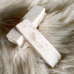 Questo poggiaposate è in marmo, con una tonalità beige chiara e una finitura leggermente ruvida. La superficie presenta leggere intrusioni e imperfezioni che conferiscono un aspetto rustico. La forma è rettangolare con bordi totalmente smussati.