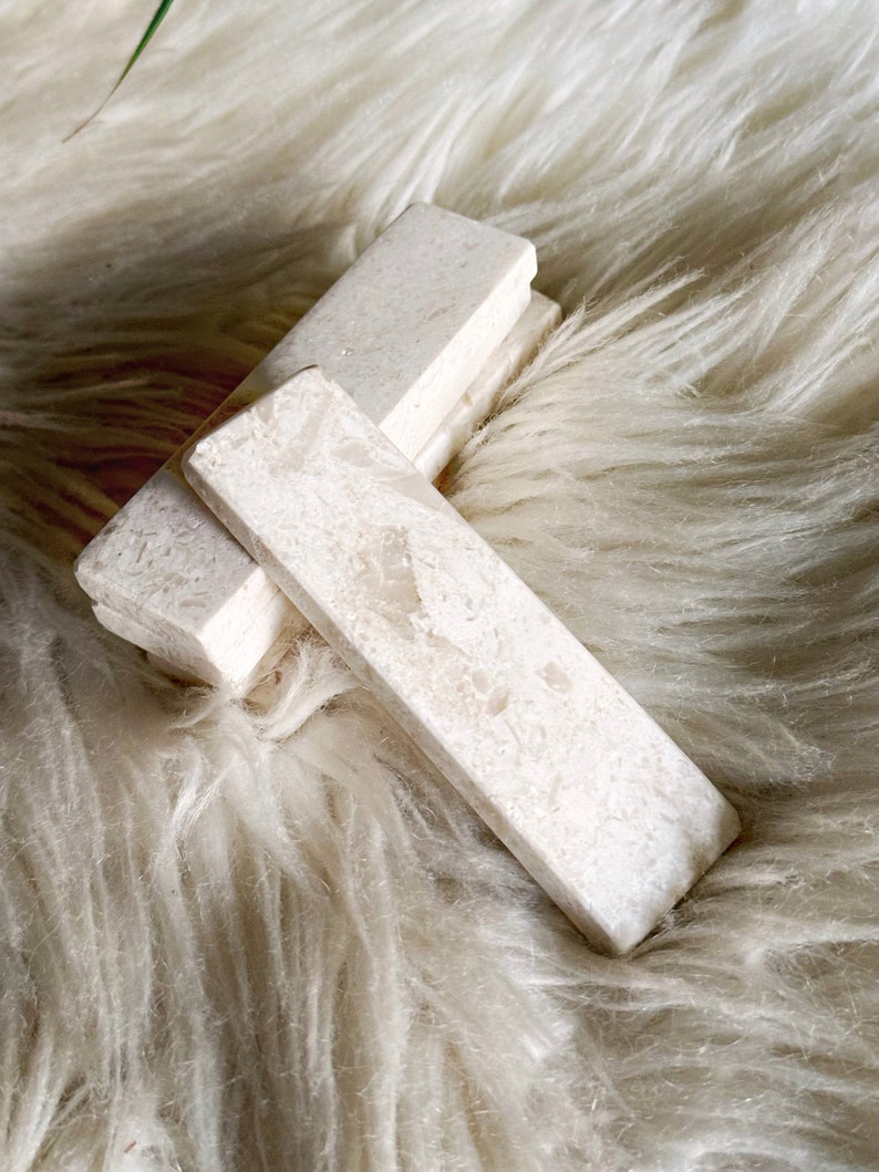 Questo poggiaposate è in marmo, con una tonalità beige chiara e una finitura leggermente ruvida. La superficie presenta leggere intrusioni e imperfezioni che conferiscono un aspetto rustico. La forma è rettangolare con bordi totalmente smussati.