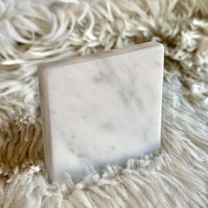 Sottobicchiere in marmo bianco Carrara dal design minimalista e raffinato. Superficie leggermente ruvida e angoli smussati. La forma quadrata e le dimensioni compatte li rendono perfetti per qualsiasi tipo di bicchiere, sia da vino che da cocktail.