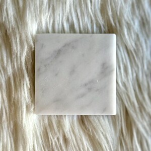 Sottobicchiere in marmo bianco Carrara dal design minimalista e raffinato. Superficie leggermente ruvida e angoli smussati. La forma quadrata e le dimensioni compatte li rendono perfetti per qualsiasi tipo di bicchiere, sia da vino che da cocktail.