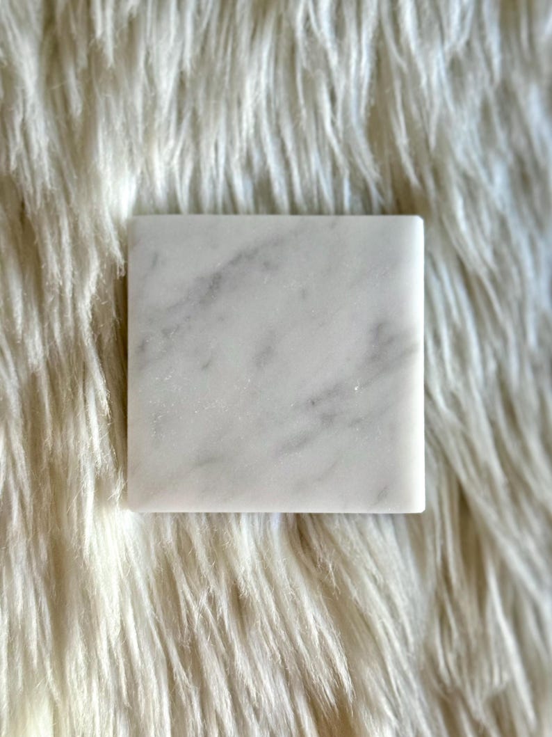 Sottobicchiere in marmo bianco Carrara dal design minimalista e raffinato. Superficie leggermente ruvida e angoli smussati. La forma quadrata e le dimensioni compatte li rendono perfetti per qualsiasi tipo di bicchiere, sia da vino che da cocktail.