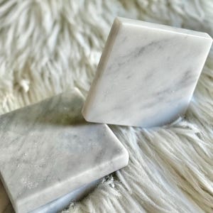 Sottobicchiere in marmo bianco Carrara dal design minimalista e raffinato. Superficie leggermente ruvida e angoli smussati. La forma quadrata e le dimensioni compatte li rendono perfetti per qualsiasi tipo di bicchiere, sia da vino che da cocktail.