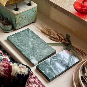 Puede incluir: Dos tablas de servir de mármol verde, una rectangular y una cuadrada, sobre una encimera blanca. Las tablas son de mármol verde con vetas blancas.