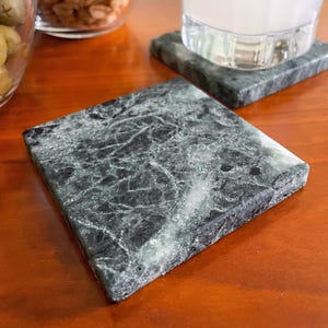 Pode incluir: Dois  quadrados de mármore verde com um padrão veteado preto e branco. Os  estão sobre uma superfície de madeira.