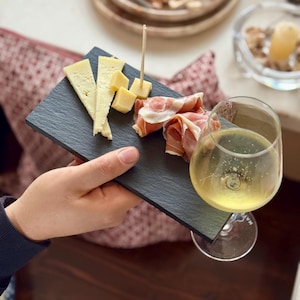 May include: A black slate serving board with a small selection of cheese and cured meat, accompanied by a glass of sparkling wine.