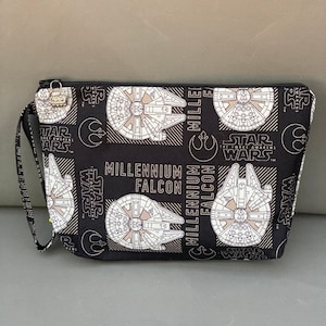 May include: Black zippered pouch with a repeating pattern of the Millennium Falcon spaceship from Star Wars. The text "Millennium Falcon" and "Star Wars" is printed on the pouch.