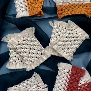 May include: Five handmade crocheted coasters with fringe. Two coasters are white with a mustard yellow stripe, two are white with a burgundy stripe, and one is all white.