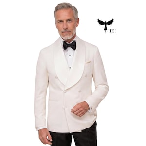 Peut inclure: Un smoking crème à double boutonnage avec un col châle, associé à un nœud papillon noir et un pantalon noir. La veste a une pochette et un design classique et formel. L'image présente un homme portant le smoking.