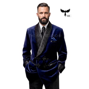 Può includere: Una giacca da smoking in velluto blu intenso con collo a scialle trapuntato nero, chiusure a alamari neri e polsini trapuntati abbinati. La giacca è indossata sopra una camicia bianca con colletto e una cravatta nera, con un fazzoletto blu nel taschino.