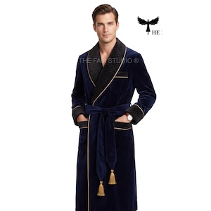 May include: A navy blue velvet robe featuring a black quilted shawl collar, cuffs, and pocket trim. The robe includes a matching tie belt with gold-colored tassels at the ends and thin gold piping along the edges. The text THE FAM STUDIO is visible.