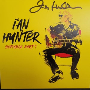 May include: A yellow album cover featuring a black and white illustration of a man playing a guitar. The album title is "IAN HUNTER DEFIANCE PART 1" in red text. The artist's signature is in black ink in the top right corner.