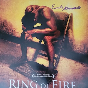 May include: A movie poster for the film "Ring of Fire: The Emile Griffith Story". The poster features a black and white photo of a man sitting on a chair, with the title of the film in large, white letters. The poster also includes the text "Can one man ever forget? Will one family ever forgive?" and "Official Selection Sundance Film Festival".