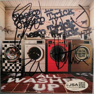 Puede incluir: Portada de álbum con tres lavadoras en una lavandería. Las máquinas son blancas, rojas y doradas, con graffiti en la pared. El texto "ALL WASHED UP" está en la parte inferior, con firmas y una pegatina de autenticación JSA.