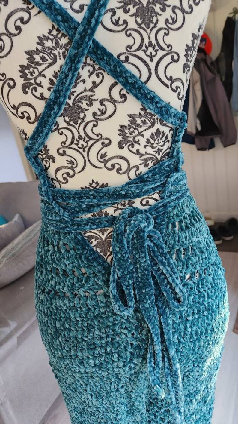 May include: A teal blue crocheted dress with a velvet texture. The dress has a criss-cross strap design in the back and ties at the waist.