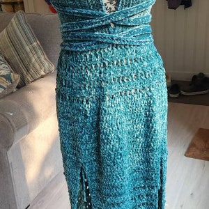 May include: A teal blue maxi dress with a deep V-neckline and a crocheted design. The dress has a wrap-style bodice and a slit in the front.