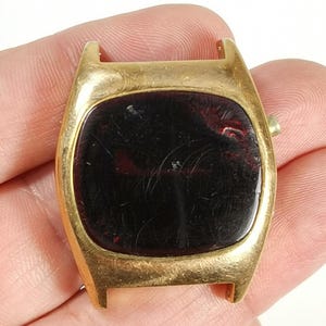 Può includere: Orologio da polso dorato con display digitale rosso. L'orologio ha una cassa rettangolare e un quadrante arrotondato.