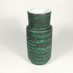May include: A dark green ceramic vase with a textured, speckled surface and horizontal bands of lighter green. The vase has a cylindrical body and a slightly flared top with a white interior. The overall design is modern and minimalist.