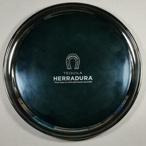 May include: A silver tray with a dark blue centre featuring the logo for Tequila Herradura. The logo includes a horseshoe with the words "Tequila Herradura" and the text "Please enjoy our handcrafted tequila responsibly."