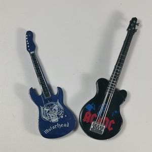 May include: Two miniature electric guitars, one blue with a skull and the text "Motorhead" and the other black with the text "AC/DC".