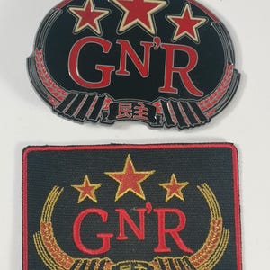 May include: Two versions of a Guns N' Roses patch. The top patch is a metal pin with a black background, red stars, and red lettering. The bottom patch is a fabric patch with a black background, gold stars, and red lettering. Both patches feature a wheat design and the text "G'N'R" and "民主".