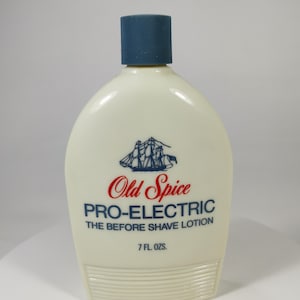 May include: An off-white Old Spice Pro-Electric before shave lotion bottle with a blue cap. The bottle has a red and blue logo of a ship and the text "Old Spice" and "Pro-Electric". The bottle contains 7 fl oz.