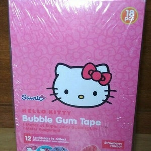 Könnte beinhalten: Eine rosa Box mit einem Hello Kitty-Design. Die Box enthält 18 Stück Hello Kitty Kaugummi-Band. Das Band ist 1 Meter lang und hat Erdbeergeschmack. Die Box enthält außerdem 12 Sammel-Lenticular-Sticker.