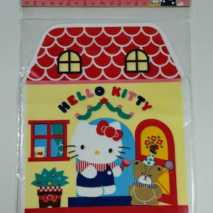 May include: A set of 5 red and yellow Hello Kitty gift bags featuring a house design with a red roof, a white door, and a window. Hello Kitty is standing in front of the house with a brown bear wearing a party hat. The text "Hello Kitty" is printed on the front of the bag.