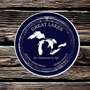 以下が含まれることがあります： 「Great Lakes」というテキストと五大湖の地図が描かれた青と白の丸いステッカー。地図の下のテキストには、「Est: Pleistocene Ice Age Sometimes Frozen Always Fresh Savvy」と書いてあります。