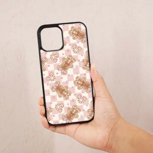 May include: A pink and white checkered phone case with a gingerbread man pattern. The gingerbread men are wearing pink bows and holding candy canes.
