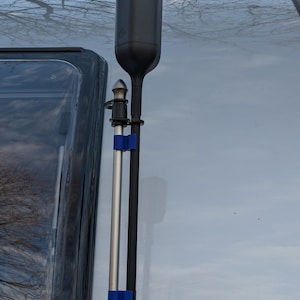 Könnte beinhalten: Eine schwarze Antenne, die auf einem silbernen Wohnmobil mit einer Teleskopstange und blauen Bändern montiert ist.
