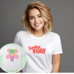 Könnte beinhalten: Weißes T-Shirt mit dem Text "Lucky YOU!" in Rot und Pink. Das Shirt hat auch ein Design einer Blume mit dem Text "Have a nice day". Das Shirt ist aus einem weichen Material.