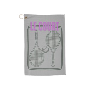 Könnte beinhalten: Graues Golftor mit weißem Rand und Tennis-Motiv. Das Handtuch trägt den Text "LE COURT" in rosa Schrift und eine Grafik mit zwei Tennisschlägern und einem Tennisball.