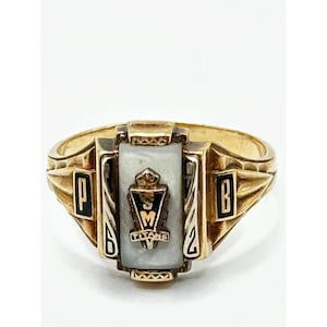 May include: A gold-colored class ring with a rectangular, off-white stone center. The ring features black and gold accents with the letters "P" and "B" on either side of the stone. The center stone has a crest and the word "TITANS".